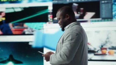 Video tavsiyeleriyle çevrili cep telefonu kullanan gülümseyen adam, internet sitelerine göz atıyor. Neşeli Afro-Amerikan erkeği boş zamanlarında akıllı telefondaki favori online videolara göz gezdirmeyi sever. Kamera A