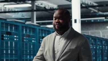 Gülümseyen bir çalışan yüksek teknoloji veri merkezinde ağları çalıştıran makinelerle yürüyor, şirketlerin veritabanlarını yönetiyor. Geniş veri işleme modülleriyle sunucu çiftliğini denetleyen yönetici, kamera B