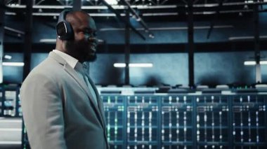 İnternet sitelerinde kullanılan donanımla veri merkezinde yürüyen kulaklık takan mutlu bir işçi. Neşeli bilişim uzmanı müzik dinlerken loş ışıklandırılmış sunucu çiftlik platformlarını, kamera A 'yı denetliyor.