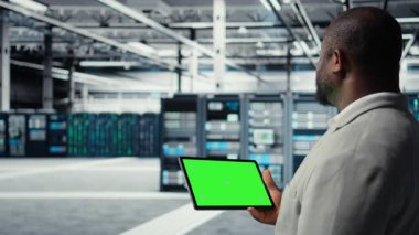 Veri merkezinde afet kurtarma planlarını geliştirmek için yeşil ekran tableti kullanan bir mühendis. Bilgi işlem uzmanı sunucu çiftliği denemelerinde başarısız olma senaryoları, model aygıtı, bozulmalar sırasında verilerin korunması, kamera A