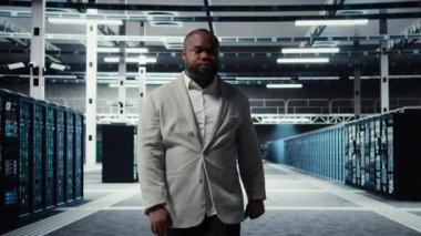 Gülümseyen bir çalışan yüksek teknoloji veri merkezinde ağları çalıştıran makinelerle yürüyor, şirketlerin veritabanlarını yönetiyor. Geniş veri işleme modülleriyle sunucu çiftliğini denetleyen yönetici, kamera A