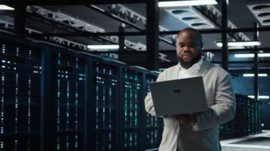 Engineer walking in data center using AI automation during maintenance session. African american server hub worker configuring deep learning models in hardware rigs, camera A