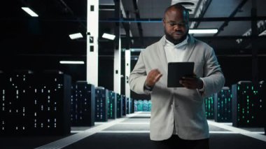 Veri merkezinde yürüyen sistem yöneticisi tabletteki altyapı performans çıktılarını analiz ediyor. Sunucu çiftlik çalışanı iş görevleri yapıyor, süper bilgisayarların ayarlarını ayarlıyor, kamera A
