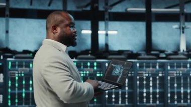 Veri merkezinde dizüstü bilgisayar kullanan, yapay zeka öğrenme modelleri kullanan bir programcı. Yapay zeka altyapı ihtiyaçlarını karşılamak için not defteri kullanan işçiler, kaynak tahsisi, kamera B