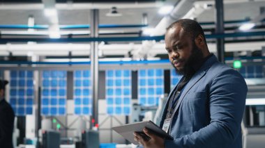 Siyah usta mühendis bir fabrikada fotovoltaik üretim hattını denetleyerek, kurumsal hedefler ve alternatif enerji standartlarını karşılamak için başarılı bir üretim süreci sağladı. Kamera B.