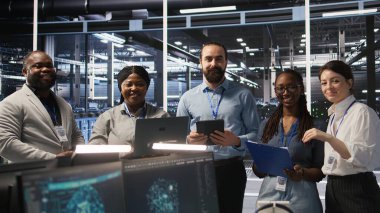 Sunucu odasında gülümseyen mühendislik ekibi altyapı tanılarını inceliyor. Veri merkezinde çalışan bilişim uzmanları, sistem bütünlüğünü ve çalışma saatlerini korumak için performans verilerini analiz ediyorlar. Kamera A