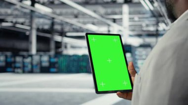 Veri merkezi bilişim uzmanı, performans gösterge panellerini gözden geçirmek için model tablet kullanıyor. Sunucu odası yöneticisi sistemleri denetliyor, krom anahtar aygıtındaki altyapıyı inceliyor, kamera A yakın plan