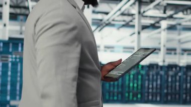 Sistem istikrarı için yazılım güncellemelerini yönetmek için tablet kullanan veri merkezindeki programcı. Sunucu odasında Afrikalı Amerikalı bir adam performansı cihazla optimize ediyor, altyapıyı yapılandırıyor, kamera B