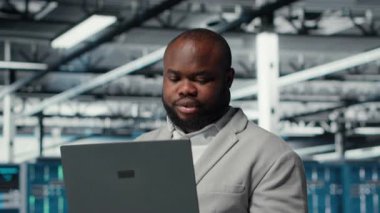 Bilgisayar bilimci veri merkezinde dizüstü bilgisayar kullanıyor, sunucu viralizasyonunu yönetiyor. Sunucu odasında not defteri kullanan Afrikalı Amerikalı bir adam, altyapının güvenilirliğini garanti ediyor, kamera B