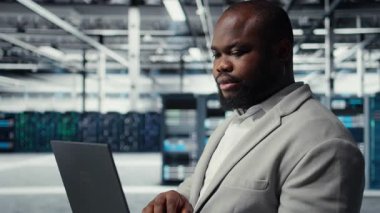 Bilgisayar kullanarak sunucu odasındaki mühendisi kapat, güvenlik yamalarını çalıştır, güvenlik duvarı yapılandırmalarını doğrula. İşçi, veri merkezinde ekipman hassasiyeti taraması yapıyor. Kamera A.