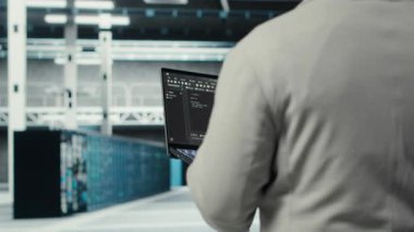 Veri merkezinde yürüyen mühendis yapay zeka görevleri için optimize edilmiş donanımı yapılandırmak için aygıt kullanıyor. Platformlarda bakım yapan adam yapay zeka hesaplaması için yük dengeleme yapıyor, kamera B