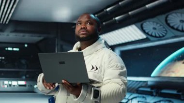 Uzay aracındaki astronot, telemetri veri analizi için dizüstü bilgisayar kullanıyor. Uzay gemisinde uzay giysisi giyen bir adam gezegen keşfi sırasında not defterindeki görev günlüklerini analiz ediyor.