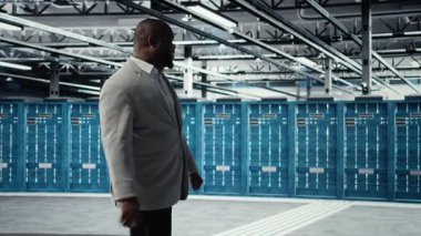 Veri merkezinde yürüyen mutlu işadamı yatırım yapmadan önce paraşütlerin kapasitesini ölçüyor. İş depolama teçhizatı için inşa edilmiş sunucu çiftliğini denetleyen neşeli yönetim yöneticisi, kamera A