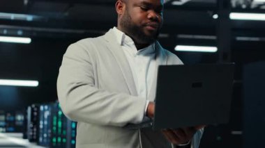 Veri merkezi sistem yöneticisi dizüstü bilgisayarda kodlama yapıyor, yazılım güncellemeleri yapıyor. Aygıt ekranına bakan sunucu odası bilişim uzmanı, altyapıyı optimize etme, yapılandırma donanımları, kamera B