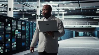 Yapay zeka otomasyon kodlarını incelemekle görevli veri merkezi sistem yöneticisi. Afrika kökenli Amerikalı bir adam sunucu merkezine girip ekipman teçhizatı ve kamera A 'yı kontrol ediyor.