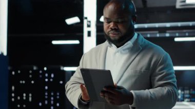 Sunucu odası teknisyeni devre dışı kalmamak için tablet kullanıyor. Veri merkezinde yürüyen bilişim uzmanı ağ performans ölçümlerini ve güvenlik kayıtlarını aygıt, kamera B kullanarak kontrol ediyor