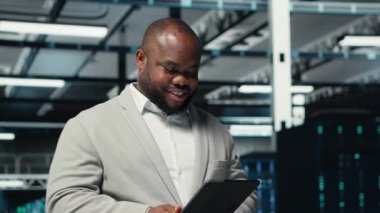 Veri merkezinde yürüyen mutlu mühendis daha hızlı işlemek için tablet üzerindeki algoritmaları inceliyor. Sunucu çiftliğinde çalışan neşeli bir çalışan altyapı kaynak optimizasyonu için kod yazarken cihaz, kamera B 'yi kullanıyor.