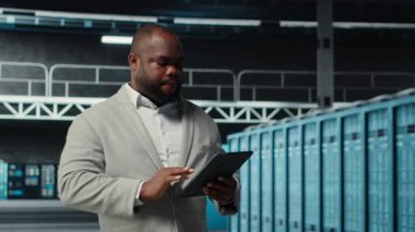 Gülümseyen veri merkezi teknisyeni tablet kullanarak yükseltilmiş sunucu rafları kuruyor. Otomasyon araçlarını kullanarak altyapı performansını izleyen iyimser sunucu odası çalışanı, kamera B