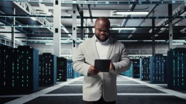 Veri merkezinde yürüyen mutlu mühendis daha hızlı işlemek için tablet üzerindeki algoritmaları inceliyor. Sunucu çiftliğindeki neşeli çalışanımız altyapı kaynak optimizasyonu için kod yazarken cihaz, kamera A 'yı kullanıyor.