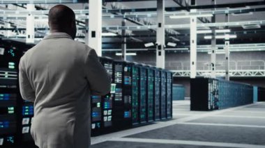 Veri merkezinde yürüyen mühendis yapay zeka görevleri için optimize edilmiş donanımı yapılandırmak için aygıt kullanıyor. Platformlarda bakım yapan adam yapay zeka hesaplaması için yük dengeleme yapıyor. Kamera A.