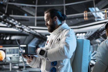 Astronot araştırmacısı navigasyon koordinatlarını doğrulamak için dizüstü bilgisayar kullanıyor, araştırma yapıyor. Uzay gemisinde kozmonot kıyafeti giyen bilim adamı uçuş sırasında yaşam destek sistemlerini izliyor