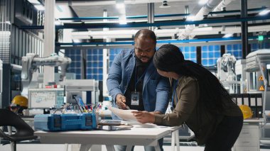 Siyahi mühendislik uzmanları ve yöneticileri bir güneş enerjisi üretim tesisindeki operasyonel iş akışlarını inceliyorlar. Yenilenebilir enerji üretimi ve gelişimi için takım çalışması entegre ediliyor. Kamera A.