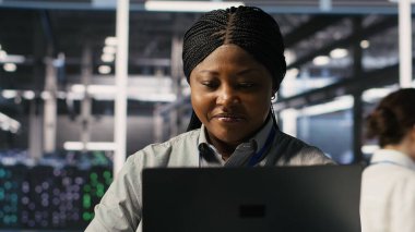 Veri merkezi sistem yöneticisi yazılım güncellemelerini tamamladıktan sonra sinirsel ağ çıktılarından memnun. IT uzmanı gülümsüyor, dizüstü bilgisayara bakıyor, sunucu merkezi donanımı optimize ediliyor, kamera A