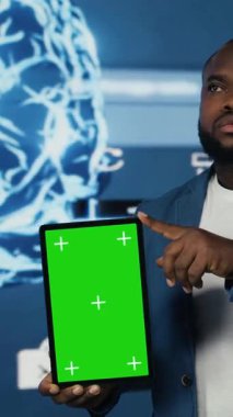 Dikey Video Afrikalı Amerikan teknoloji mühendisi algoritmik verileri, dijital görsellerle çevrili bir tablet tutarak, modelin yanında inceledi. Modern bir ortamda yapay zeka teknolojisi ve sinirsel ağlar