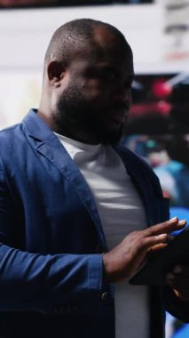 Dikey Video Genç siyahi kişi mobil cihazlar aracılığıyla küresel sosyal ağlara bağlanıyor, gösterge panelinde çevrimiçi platformlar açıyor. Sosyal medyada iletişim ve çoklu görev. Kamera B.