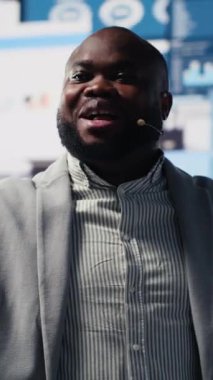 Dikey Video Afrikalı Amerikalı konuşmacı iş adamı canlı izleyicilerle dinamik bir sunum sunuyor ve bir kongrede verimli bir strateji geliştiriyor. İş etkinliğinde fikirler ve tahminler