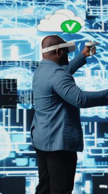 Dikey Video Siyah iş adamı, dijital veri işleme ortamında veri bilimi, otomasyon ve yapay zeka etiğini keşfetmek için ileri teknoloji VR kulaklık araçları kullanıyor. Makine öğrenimi üzerine çalışır