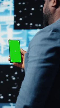 Dikey video odaklı siyah bilişim uzmanı, dijital yapay zeka ortamında duran yeşil ekranlı telefona bakıyor. Büyük veri otomasyonu için derin öğrenme görevleri çözülüyor