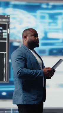 Dikey Video Afrikalı Amerikalı geliştirici, programlama ve otomasyon üzerine çalışıyor, arkasında fütürist bir arayüzü olan bir dizüstü bilgisayarda kodluyor. Teknoloji profesyoneli yapay zeka ve kod parçacıklarının dünyasında gelişiyor.