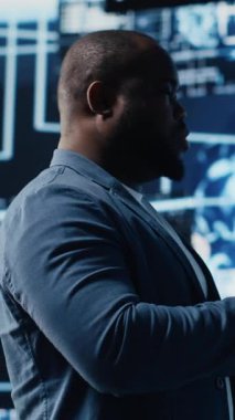 Dikey Video Siyah erkek bilişim mühendisi torpido gözündeki dijital yapay zeka arayüzünü inceleyerek nöral ağları, bilimi ve algoritmik düşünceyi sembolize ediyor. Yüksek teknoloji makine öğrenimi için sibernetik