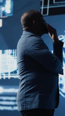 Dikey Video Afrikalı Amerikalı iş adamı dijital yapay zeka arayüzü üzerinde çalışıyor, nöral ağları, veri bilimini ve algoritmik düşünceyi sembolize ediyor. Yüksek teknolojili fütüristik yenilik için sibernetik