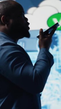 Dikey Video Afrikalı Amerikalı bilişim uzmanı akıllı telefonuyla bir teknisyeni arıyor, sinirsel ağlar üzerinden otomasyon hakkında konuşuyor. İşadamı kodlama ve veri işleme hakkında konuşuyor. Kamera.