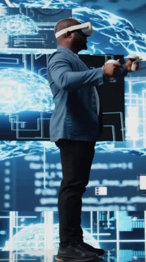 Dikey Video Genç Afrikalı Amerikalı mühendis VR kulaklık programlama ve analizlerine odaklanmış, nöral ağlar ve yapay zeka veri görselleştirmesi ile çevrelenmiş. Yenilik ve sibernetik. Kamera A.