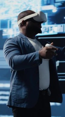 Dikey Video Genç Afrikalı Amerikalı mühendis VR kulaklık programlama ve analizlerine odaklanmış, nöral ağlar ve yapay zeka veri görselleştirmesi ile çevrelenmiş. Yenilik ve sibernetik. Kamera B.