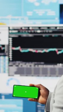 Dikey Video Afrikalı Amerikalı iş adamı, KPI metriklerinin yanındaki yeşil ekranı kullanarak şirketin yüksek kalitede bir yaşam sürmesini sağlıyor. Genç girişimci, fintech projeksiyonlarını inceliyor. Kamera.