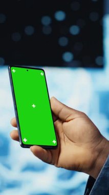 Dikey video odaklı siyah bilişim uzmanı, dijital yapay zeka ortamında duran yeşil ekranlı telefona bakıyor. Büyük veri otomasyonu için derin öğrenme görevleri çözülüyor