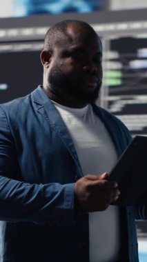 Dikey Video Afrikalı Amerikalı geliştirici, programlama ve otomasyon üzerine çalışıyor, arkasında fütürist bir arayüzü olan bir dizüstü bilgisayarda kodluyor. Teknoloji profesyoneli yapay zeka ve kod parçacıklarının dünyasında gelişiyor.