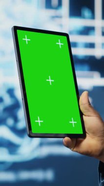 Dikey Video BT uzmanı kroma anahtarının yanındaki algoritmik verileri inceliyor, ileri teknoloji ortamında fütürist dijital görsellerle tablet kullanıyor. AI akıllı teknoloji ve sinirsel ağlar
