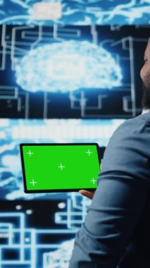 Dikey Video BT uzmanı kroma anahtarının yanındaki algoritmik verileri inceliyor, ileri teknoloji ortamında fütürist dijital görsellerle tablet kullanıyor. AI akıllı teknoloji ve sinirsel ağlar