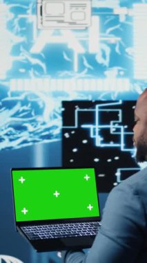 Dikey Video Siyah Erkek Mühendis, yapay zeka beyin gelişimine ve derin öğrenmeye batmış öngörücü analitiklerin yanında krom anahtar ekranlı dizüstü bilgisayar gösteriyor. Yüksek teknoloji sibernetik algoritmalar. Kamera A.