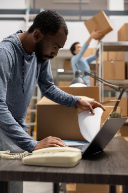 Siyah depo çalışanları, yerel bir markanın paketlerini ve sipariş işlemlerini yöneterek, endüstriyel depolama odasında verimli dağıtım ve yerel teslimatla ilgileniyorlar. Küçük işletme.