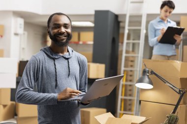 Afro-Amerikalı bir adam ürün sevkiyatını denetliyor ve lojistik siparişi veriyor. Küçük ölçekli fabrika operasyonlarında raflarda kutular yığılmış halde çalışıyor. Mal ve işlem emirleri..