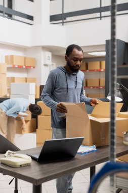 Siyah depo çalışanları, yerel bir markanın paketlerini ve sipariş işlemlerini yöneterek, endüstriyel depolama odasında verimli dağıtım ve yerel teslimatla ilgileniyorlar. Küçük işletme.
