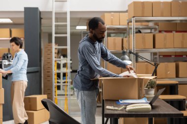 Dağıtım merkezi için sevkiyat lojistiğini inceleyen zenci bir çalışan yerel bir küçük işletme için depo malzeme odasında nakliye alanında çalışıyor. Özel siparişler yönetiliyor.