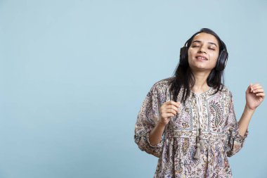 Neşeli genç insan kulaklıkla müzik dinleyip dans ediyor, şarkı söylüyor ve mavi arka planda hareket ediyor. Mutlu mutlu kız kulaklık takıyor ve eğleniyor..