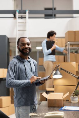 Depo çalışanı emirleri koordine etmek ve dağıtım faaliyetlerini sağlamak için dizüstü bilgisayar kullanıyor. Küçük işletme lojistik süreci. Bantlanmış kutular organize malzeme odasında hazırlanıyor..